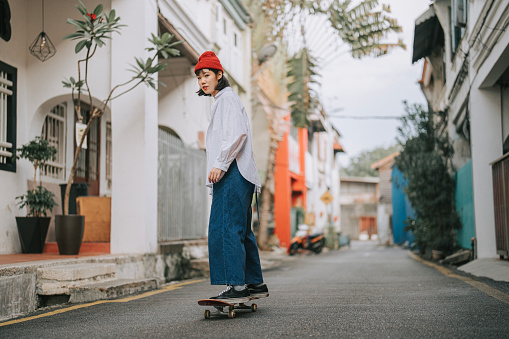 asian chinese young woman skateboarding in penang old town alley street