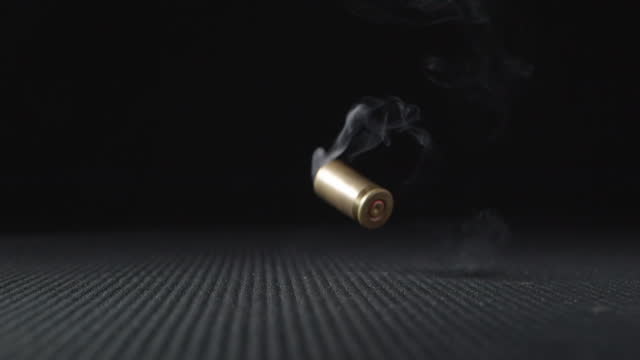 Slow motion shot of empty bullet shells fall down on a black background.