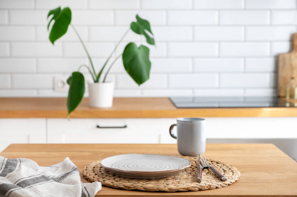 istock Wooden table top with plate and cup for breakfast against blurred white kitchen with cutting board and monstera plant in scandinavian style 1496294172