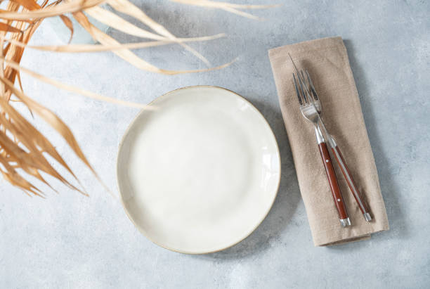 istock Table setting with ceramic plate and cutlery and dry palm leaf on light background. Minimal summer style concept. 1496294244
