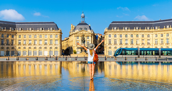 Happy woman tourist with arms raised in France- Bourse square with water mirror,  Bordeaux city landscape