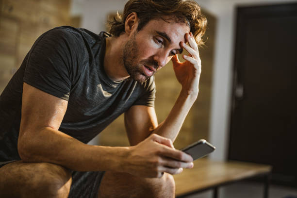 istock Exhausted sweaty man using cell phone at gym's dressing room. 1496296834