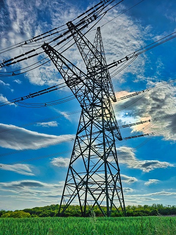 A low angle of an electrical tower against a cloudy blue sky on a sunny day