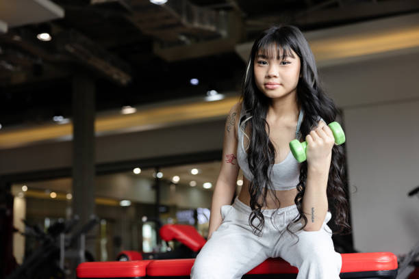 Teenage girl playing with dumbbell workout in the gym to have a good health shape. Gen Z lifestyle stock photo