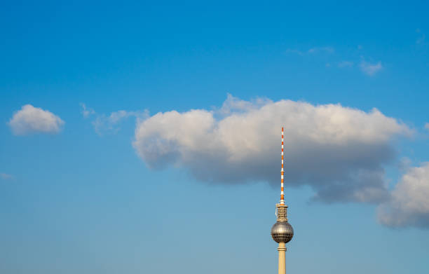 The iconic Fernsehturm in Berlin reaches high, surrounded by a clear blue sky and scattered clouds during the day.