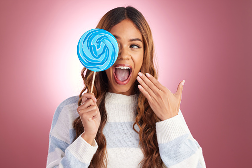 Excited, woman and lollipop candy in a studio with a female feeling happiness from sweets. Smile, surprise and happy model with a sweet dessert treat with isolated pink background and sugar snack
