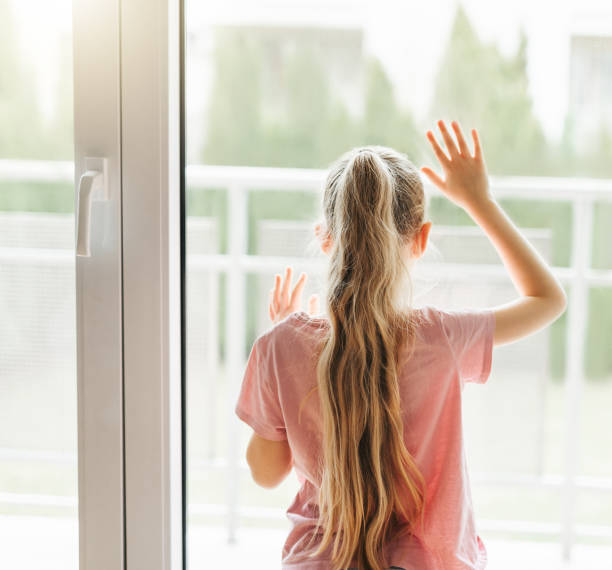 istock Sad little girl looking through  window at home. 1496303073