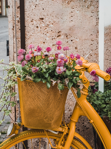 Basket with pink flowers on a yellow bike. Urban street decor. Bright bicycle close-up