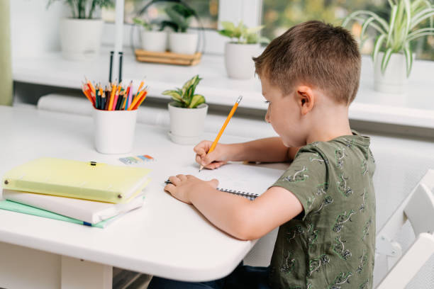 istock Back to school. Kid boy studying at home with book, writing in notepad and doing school homework. Thinking caucasian child siting at table with notebook. Distance learning online education 1496310574