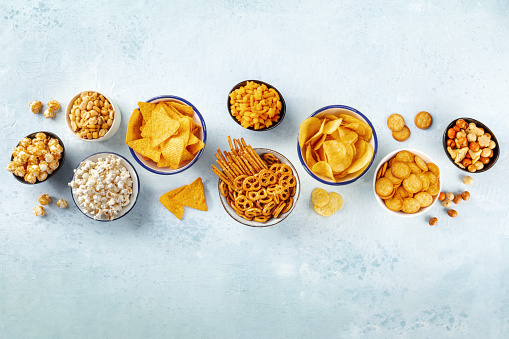 Salty snacks, party mix. An assortment of crispy appetizers, shot from above on a slate background with copy space. Potato and tortilla chips, crackers, popcorn etc