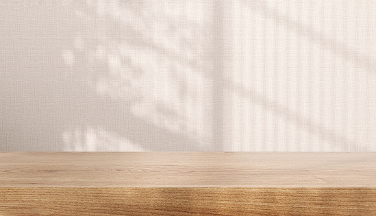 Blank brown wooden counter table in soft sunlight, leaf shadow on beige cream fabric texture wallpaper wall