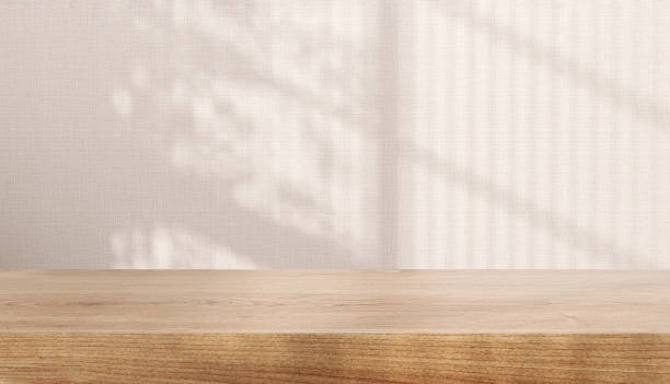 Blank brown wooden counter table in soft sunlight, leaf shadow on beige cream fabric texture wallpaper wall stock photo