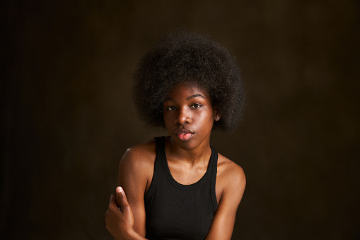 Portrait of a beautiful young black woman with curly black afro hair. She is with her arms crossed