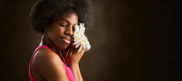 young woman with afro hair smelling a daisy with her eyes closed to better perceive the aroma stock photo