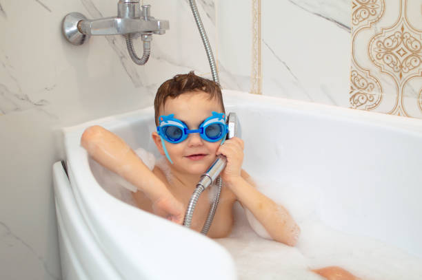istock Funny child is having fun bathing, sitting in white bath with soap and shampoo foam and washing his head with his hair. Shampoo, hair care product and soap for children. Concept of health and hygiene 1496314333