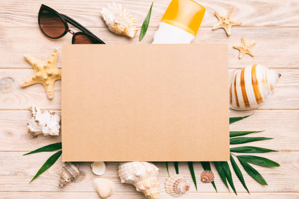 istock Summer time concept with blank greeting card and blank craft paper on colored background. Seashells from ocean shore in the shape of frame separated with space for text top view 1496314504