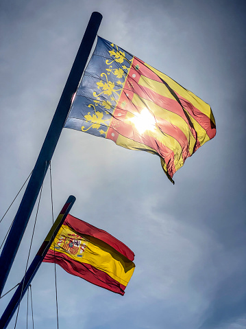 Back lit view of Valencian and Spanish flags waving outdoors.