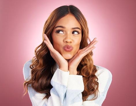 Beauty, kiss and hands on face of a woman in studio on gradient pink background feeling silly, cute or goofy. Headshot of young female fashion or skincare model looking playful, excited or flirting