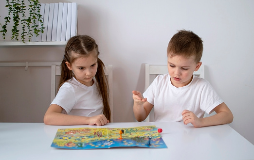 Children are playing a board game. Portrait of a boy and a girl sitting at a table playing with colorful cubes. The concept of child development.