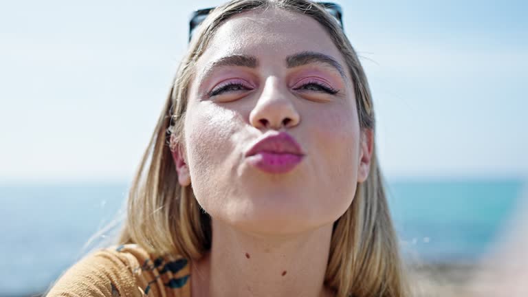 Young blonde woman making selfie by the smartphone kissing at seaside