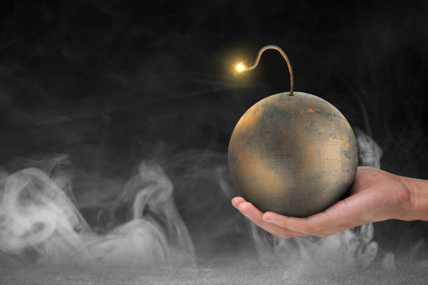 A human hand holding a ball bomb with a burning fuse on dark background