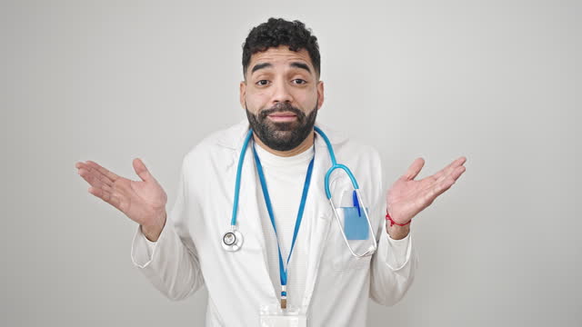 Young hispanic man doctor standing clueless over isolated white background