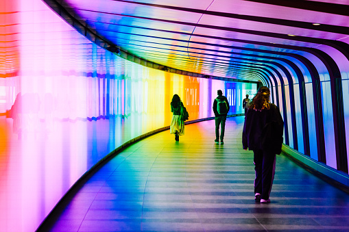 London, UK - 5 June, 2023: a crowd of people and commuters walking through an illuminated, multi-colored, futuristic underground tunnel in central London, UK.