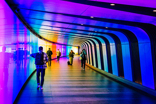 London, UK - 5 June, 2023: a crowd of people and commuters walking through an illuminated, multi-colored, futuristic underground tunnel in central London, UK.