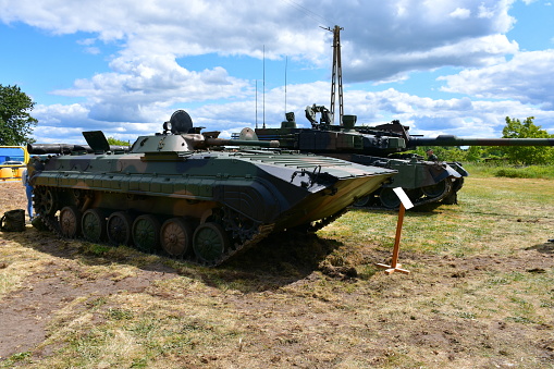 A close up on two heavy armoured tanks or trucks used by the military and painted in camo colors displayed during a military fair or picnic seen on a sunny summer day on a vast field