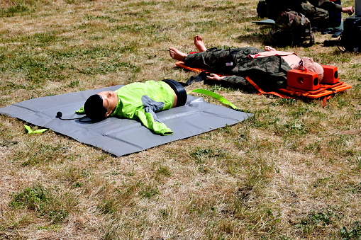 A close up on two dummies or dolls used to practice CPR and first aid, laying on some cloth and plastic supports spotted during a military fair or picnic organized in Poland in summer