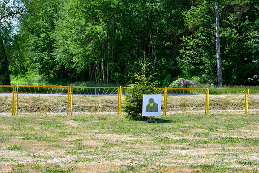 A view of a target being a part of a temporary set up shooting range located next to a small tree, some yellow fence and a dense forest or moor seen during a military picnic in Poland