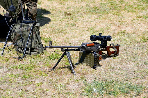 A close up on a modern machine gun with a scope used by the military in war scenarios seen in the middle of a dry field on a sunny summer day during a military fair