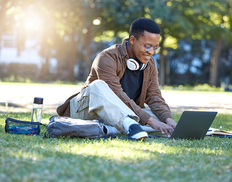 Black man, park studying and laptop work in a campus garden with a smile and lens flare, Outdoor, happiness and online elearning with a textbook of a student busy with exam study on university grass