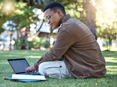 Black man reading, park and laptop work in a garden with a education book and lens flare, Outdoor, happiness and online elearning with a textbook of a student busy with exam study on university grass