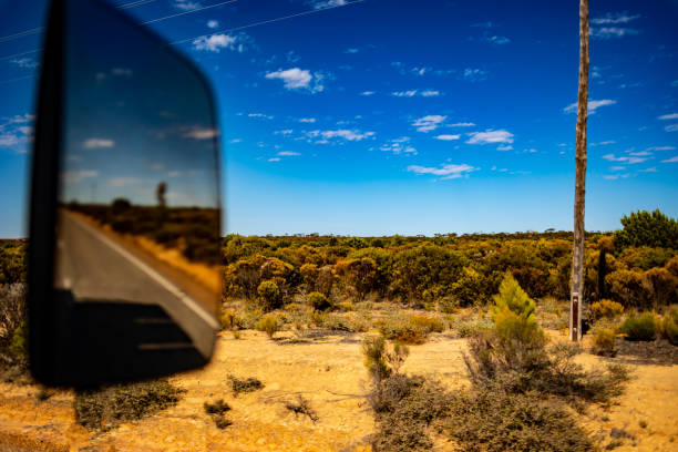 A serene drive through Katherine reveals a beautiful sunset reflected in the side mirror of a vehicle, capturing the vibrant colors of dusk against the backdrop of Northern Territory's landscape.