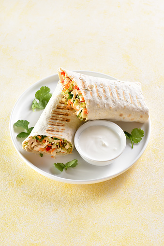 Tortilla wraps with chicken and fresh vegetables on plate over light background. Close up view