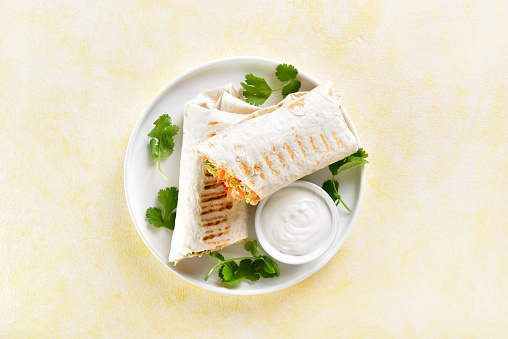 Tortilla wraps with chicken and fresh vegetables on plate over yellow background. Top view, flat lay