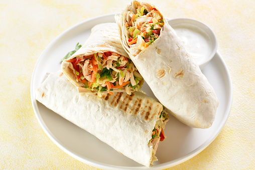 Tortilla wraps with chicken and fresh vegetables on plate over light background. Close up view