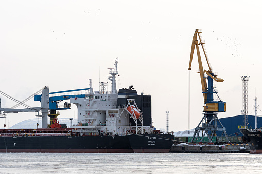 Riga, Latvia - February 9, 2021: bulk cargo ship under port crane bridge