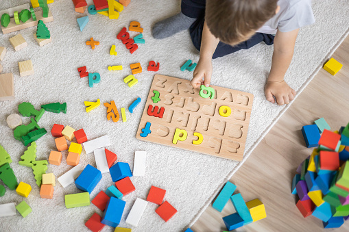 Male kid playing with wooden eco friendly alphabet letters board on table top view. Intellectual game preschool primary education early development font characters for learning reading and writing