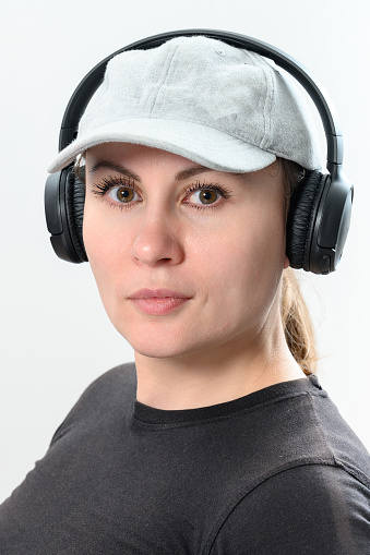 Portrait of a girl on a white background with wireless headphones and a cap on her head, copy space and place for advertising.