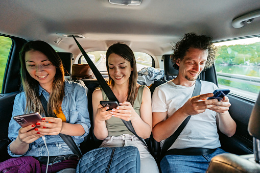 Three young friends using their phones while riding in the backseat of the car through Bosnia.