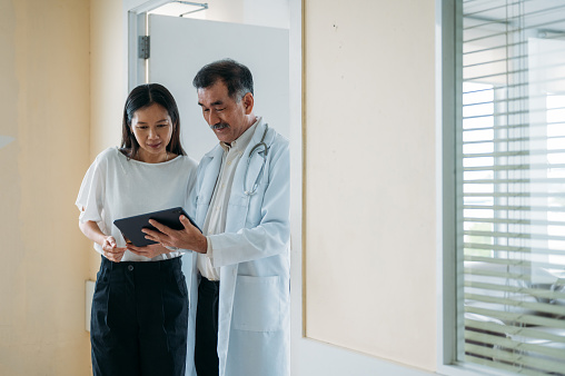 Shot of an Asian male doctor discussing something on a digital tablet with a female patient in a clinic.