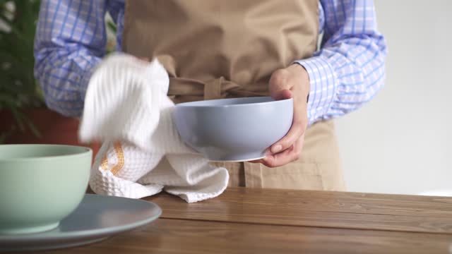 Female hands wipe the dishes with a white waffle weave towel. woman in a beige apron in a rustic kitchen wipes the washed dishes