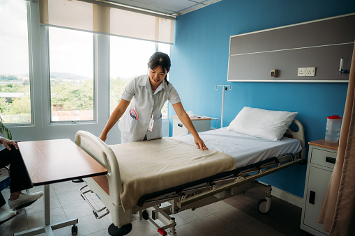 Hospital Ward: Beautiful, Professional Asian Nurse Working, Doing Bed, Cleaning Room After Happy Healthy Patients Recover and are Discharged Under Treatment of the Best Doctors. Sunny Room