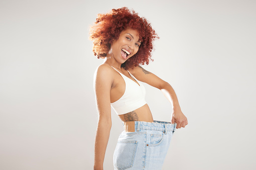 Weight loss concept, a happy woman wearing loose blue jeans showing off her weight loss, isolated on white background with copy space