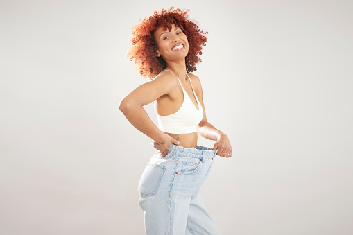 Weight loss concept, a happy woman wearing loose blue jeans showing off her weight loss, isolated on white background with copy space