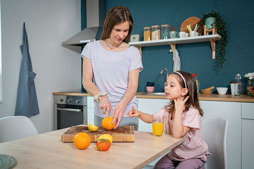 Caucasian toddler girl makes company to her mother while she preparing her a healthy snack