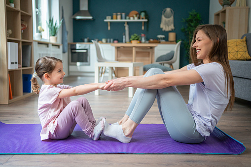 Active and healthy young Caucasian woman, doing home workout with her daughter