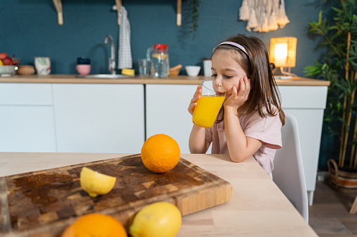 Caucasian toddler girl drinking orange juice in the kitchen